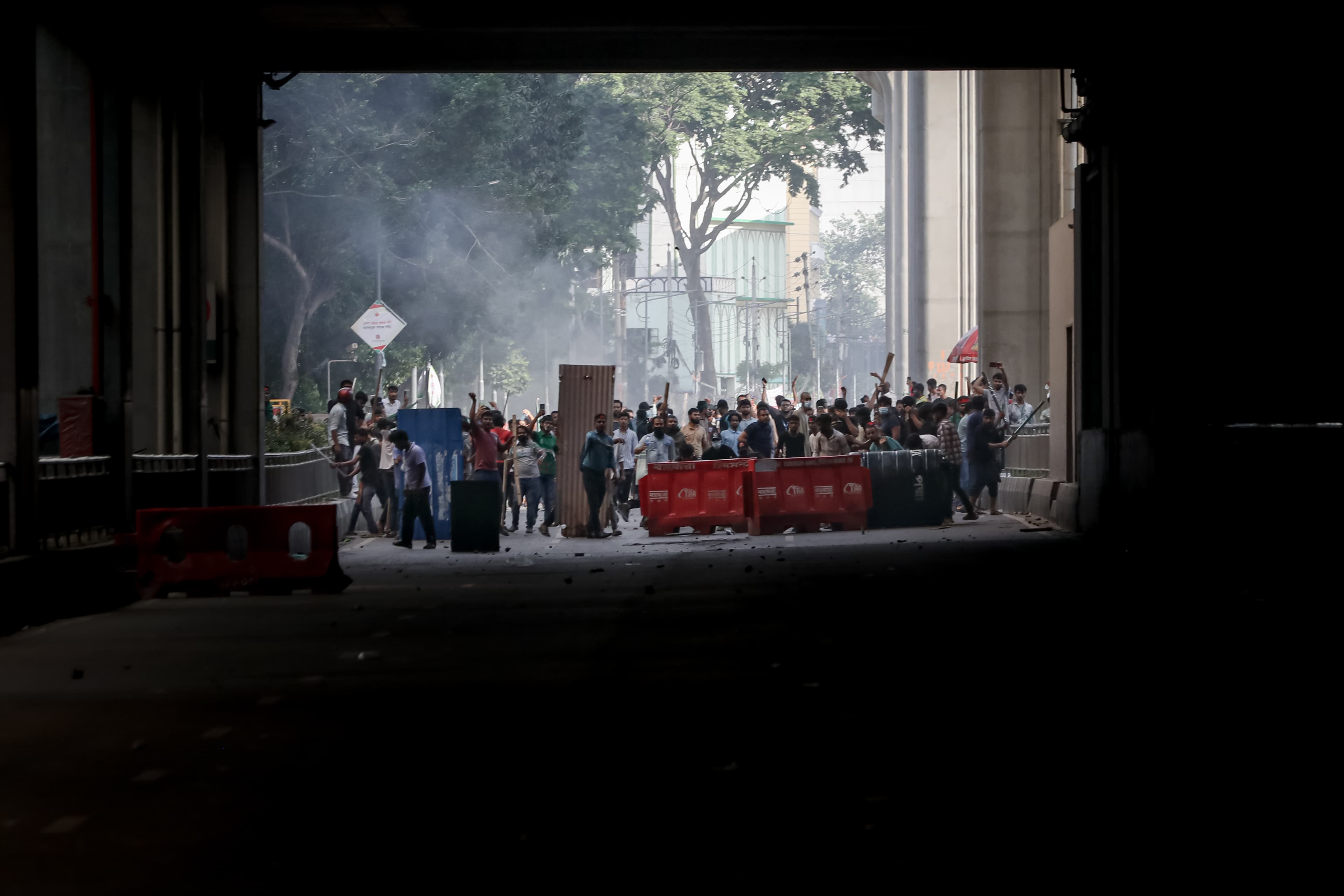 A crowd gathered in the light beyond a dark underpass, many with raised hands, during a street protest.